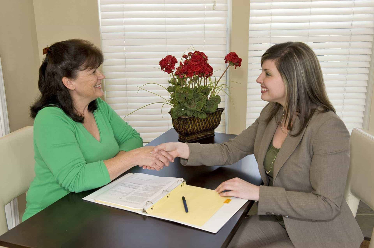 Two women shaking hands over a desk.