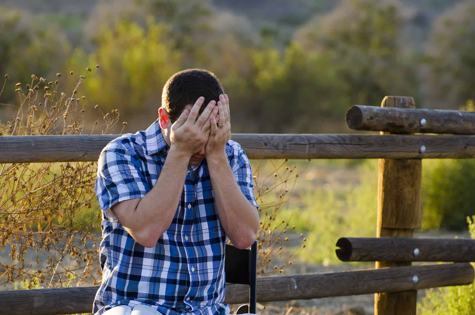 Man with hands covering his face sitting outdoors.