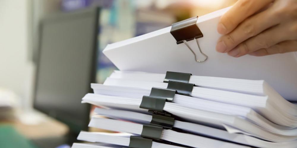 Stacks of papers attached together with binder clips and a computer monitor in the background