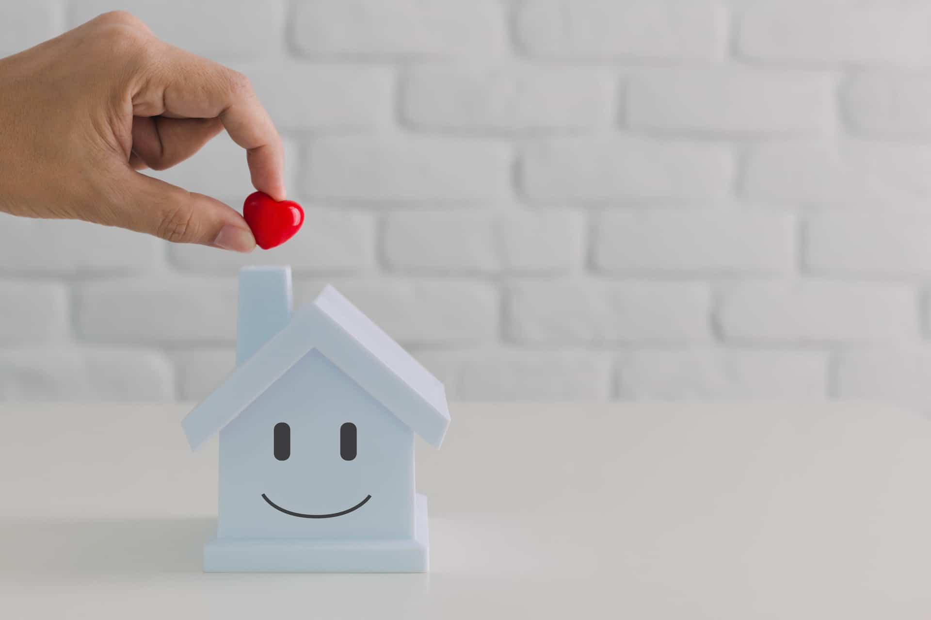 Hand putting red heart in to house piggy bank with smiling face