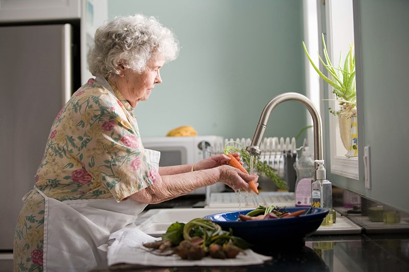 elderly woman washing dishes in home